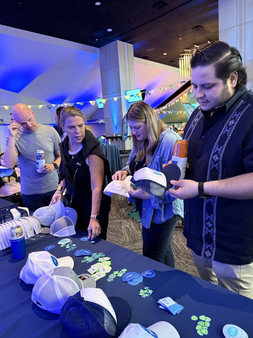 Guests choosing caps and patches at an onsite hat bar table during a corporate event