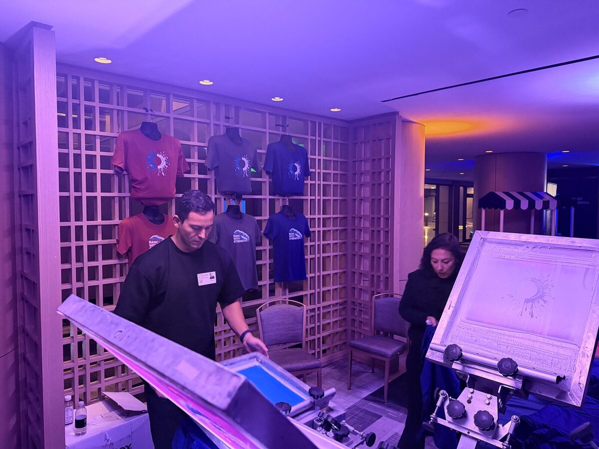 Operator preparing a screen press beside a display wall of printed shirts in a hotel lobby