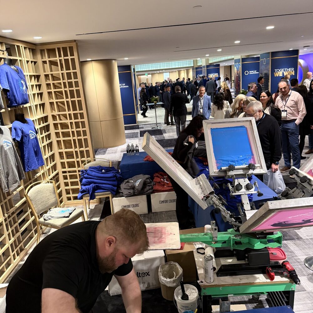Onsite print station with folded shirts and a display shelf at a business conference